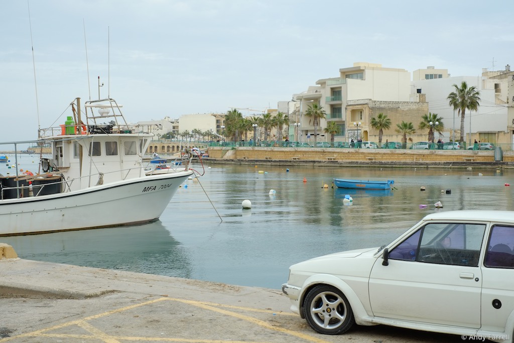 boat on, and car next to, Marsaskala bay