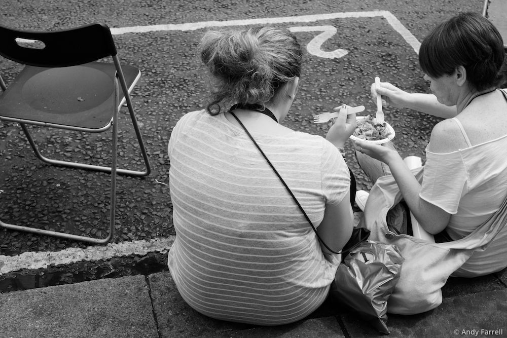 two women sitting on the kerb and eating