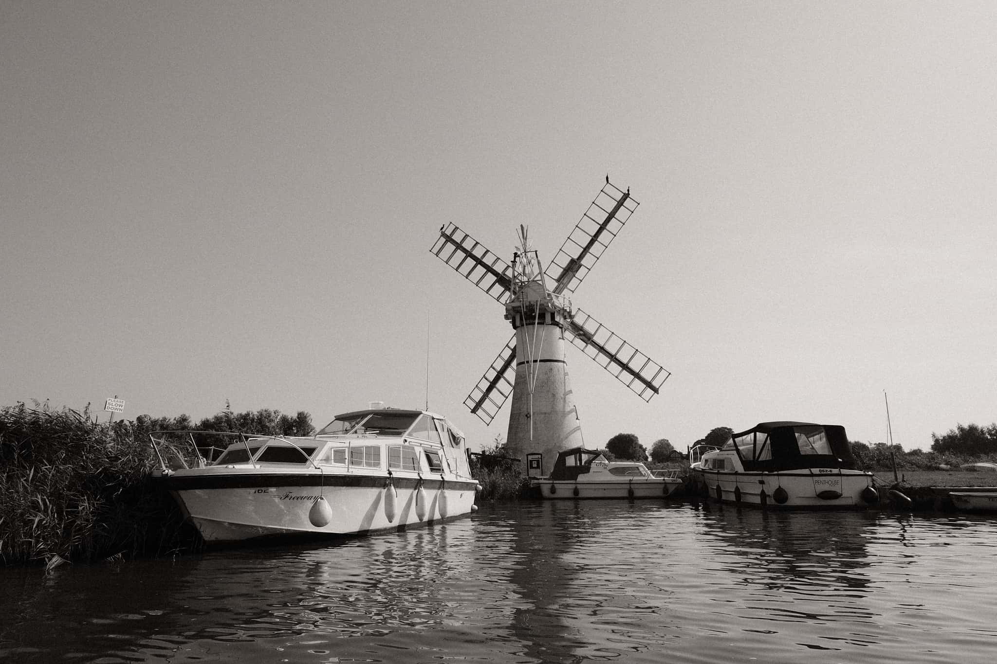 Various boats moored next to a windmill.